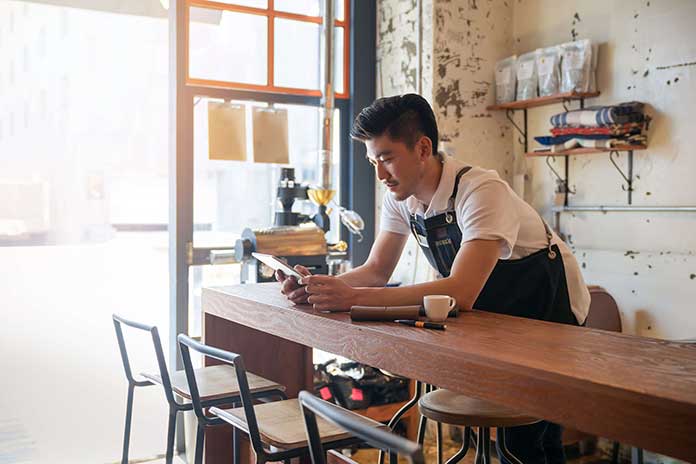 Person wearing an apron holding tablet leaning on table in a cafe