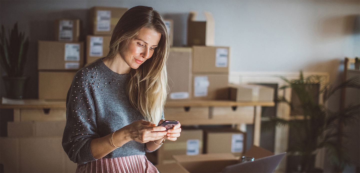 Lady with lots of packaged boxes behind her looking at her mobile phone. Lady with lots of packaged boxes behind her looking at her mobile phone.
